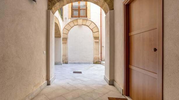 Un pasillo con puerta de madera, entrada en arco y suelo de baldosas.