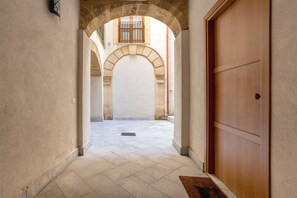 Un pasillo con puerta de madera, entrada en arco y suelo de baldosas.