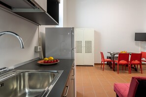 Una cocina con un lavamanos de acero inoxidable, un refrigerador blanco y una zona de comedor con sillas rojas y una mesa.