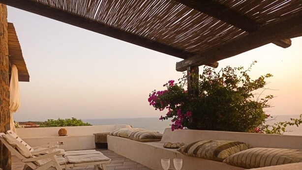 Eine Terrasse mit Liegestühlen und einer Sitzecke, ein Tisch mit Gläsern und Blick aufs Meer.
