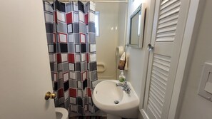 A bathroom with a white sink, a mirror, a towel, and a shower curtain with a geometric pattern. - Main Floor Suite (Stettler)