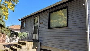 A single-story house with a front door, a small porch, and a window with blinds. - Main Floor Suite (Stettler)