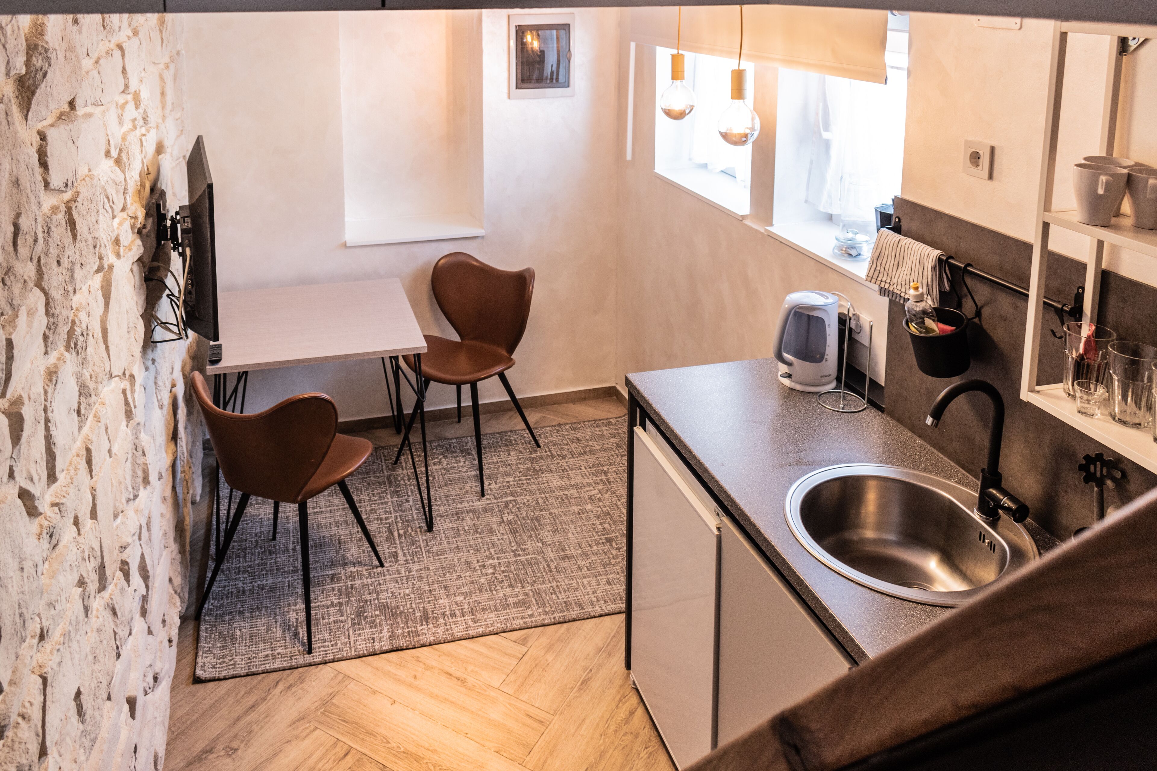 A compact kitchen with a herringbone floor pattern, a built-in sink, and a small dining area with two chairs.