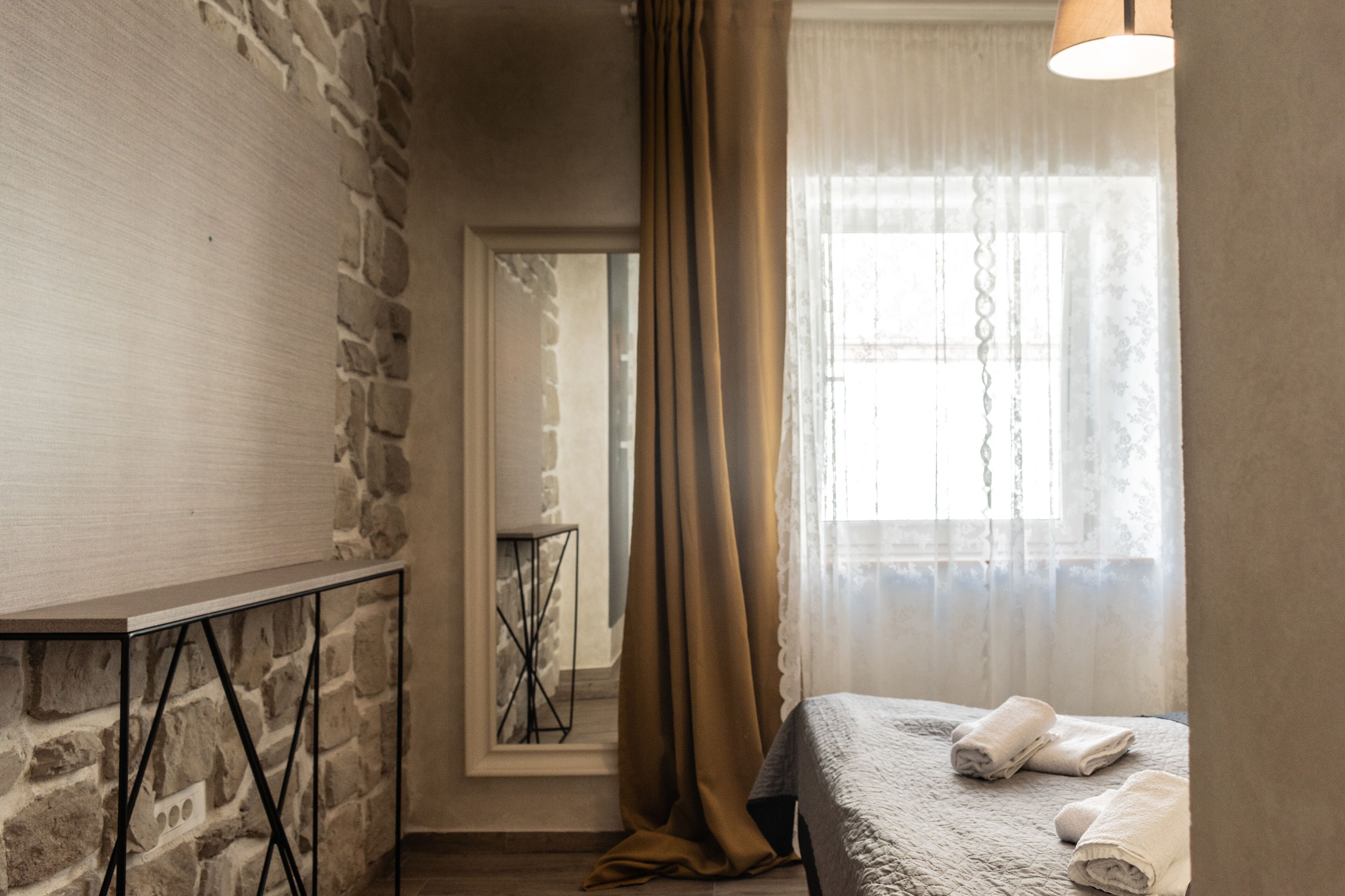 Un dormitorio con pared de piedra, una cama con cubrecama blanco y una ventana con cortinas de gasa.