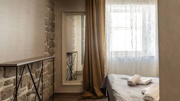 Un dormitorio con pared de piedra, una cama con cubrecama blanco y una ventana con cortinas de gasa.