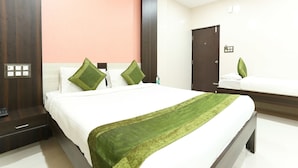 A hotel room with a bed, a nightstand, a dresser, and a bathroom with a sink and mirror. - Hotel Habitat Comforts (Bengaluru)