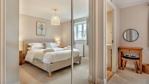 A bedroom with a bed, bedside tables, a mirror, and a small wooden cabinet. - Three bedroom dog friendly holiday cottage in the Cotswolds - Cedar Cottage (Bourton-on-the-Water)