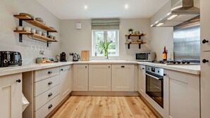 A modern kitchen with wooden flooring, built-in appliances, and open shelving. - Three bedroom dog friendly holiday cottage in the Cotswolds - Cedar Cottage (Bourton-on-the-Water)