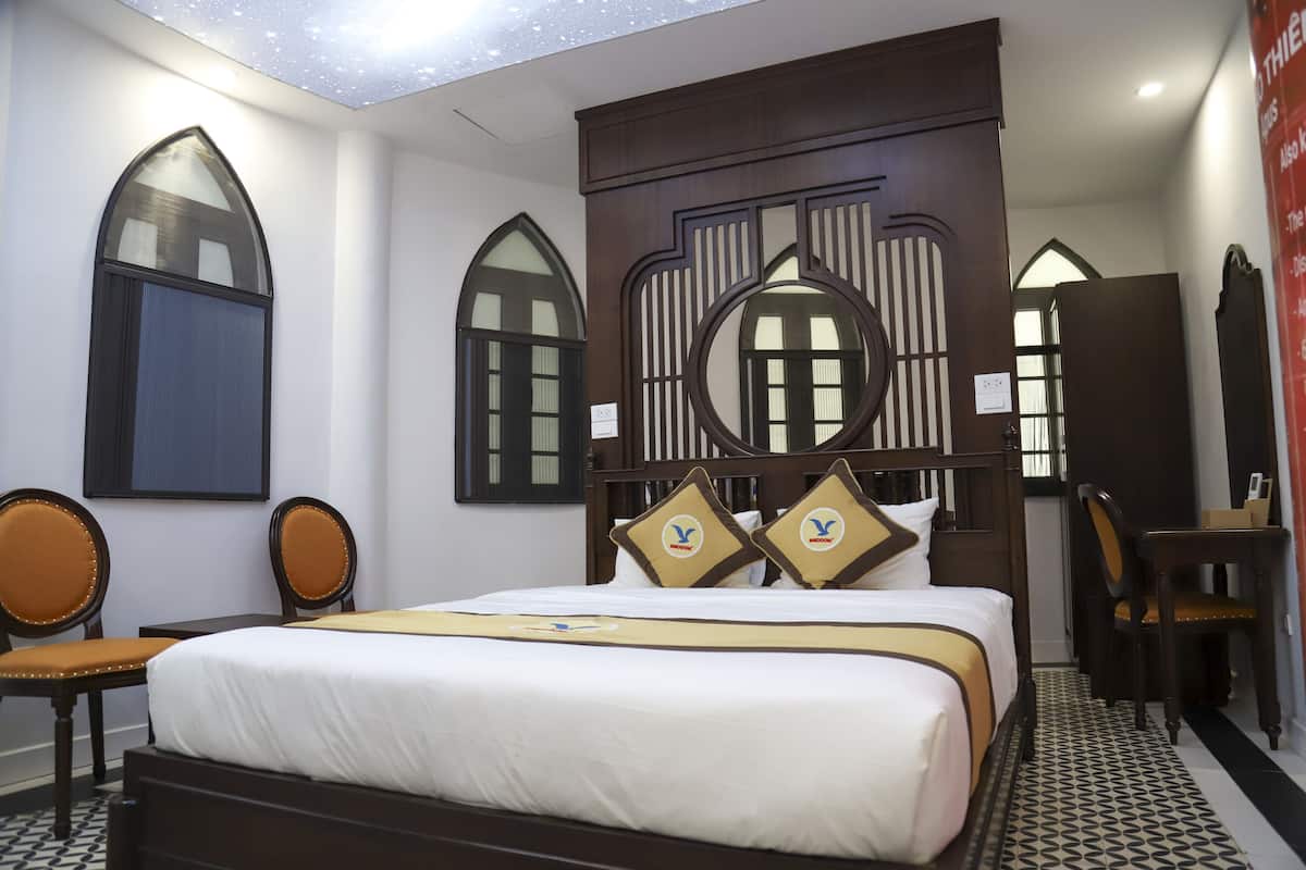 A hotel room with a bed, two chairs, a desk, and a decorative wall panel.