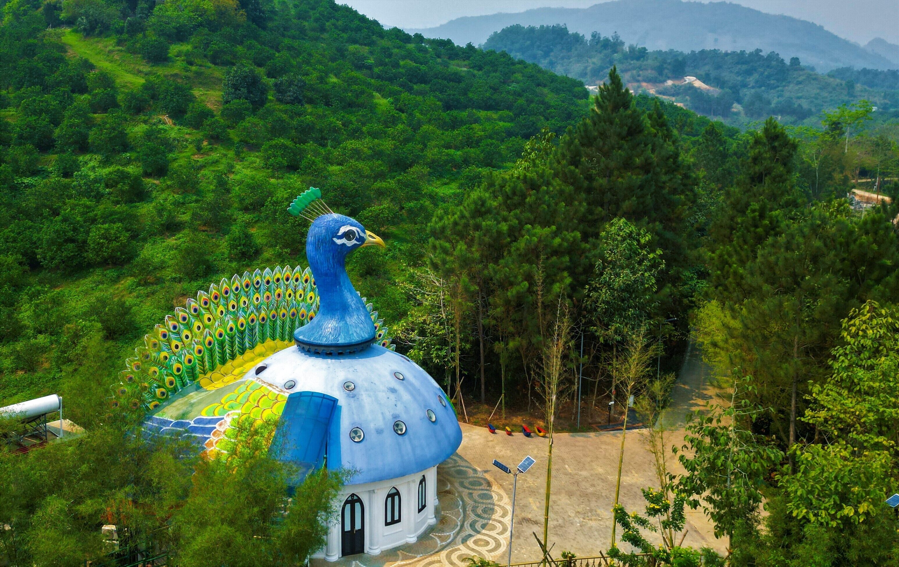 A peacock-shaped building with a dome, surrounded by lush greenery and hills.