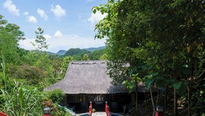 A traditional thatched-roof building with a red staircase leading up to a pool, surrounded by lush greenery and mountains in the background. - MEDDOM Park (Thung Nai)