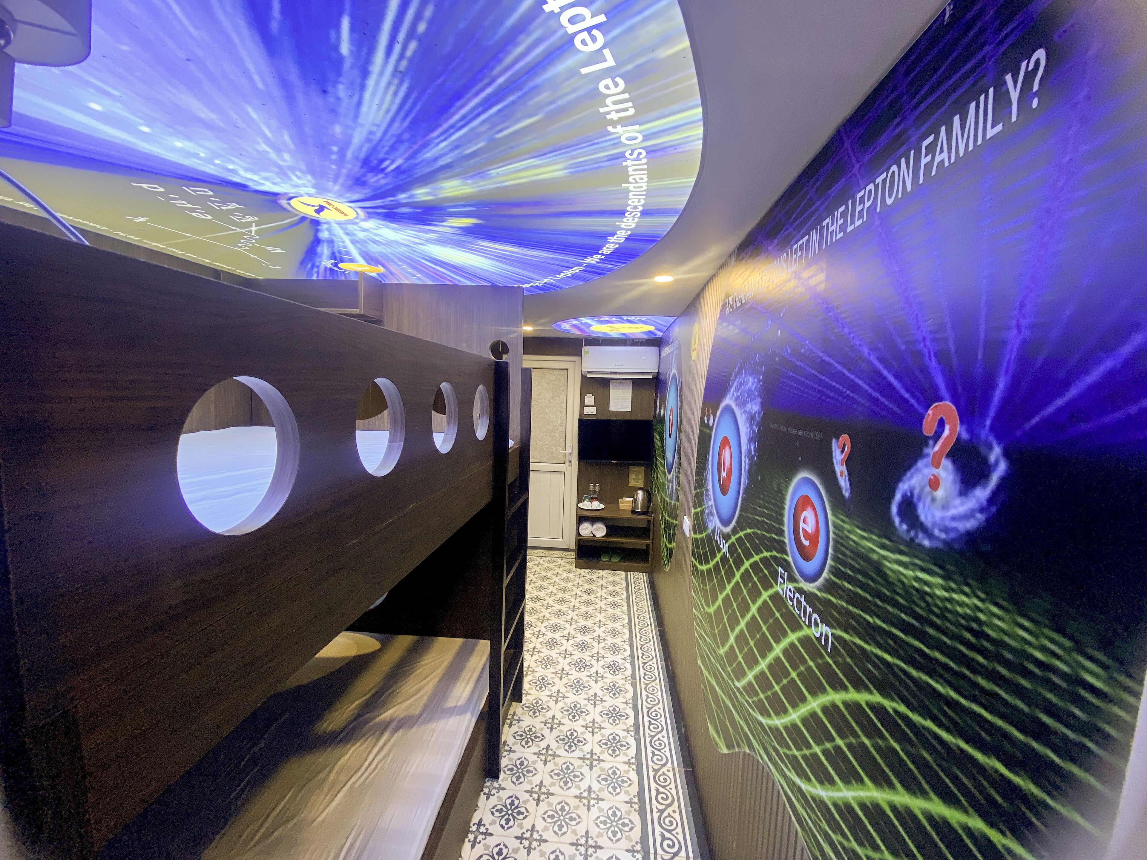 A hallway with a modern design, featuring a wooden bench with circular cutouts and a wall with a projection of the Lepton Family.
