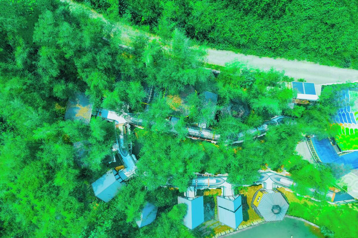 An aerial view of a residential area with modern houses, a winding road, and a park with a circular structure.