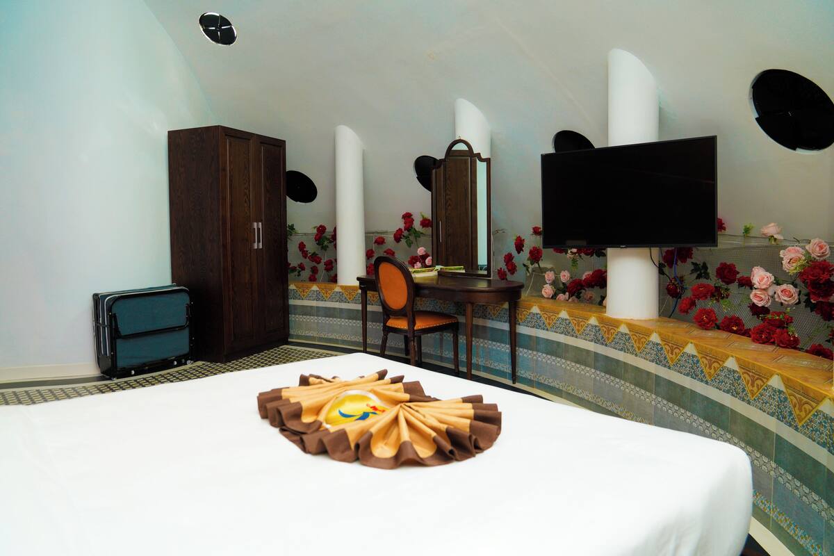 A hotel room with a bed, a desk, a chair, a wardrobe, a television, and decorative flowers on the wall.