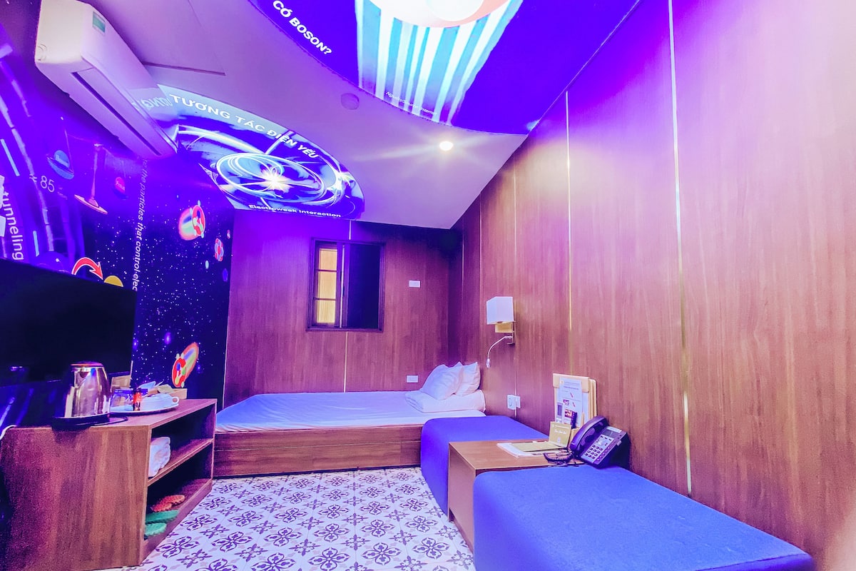 A room with a bed, a desk, a shelf, and a wall-mounted TV.