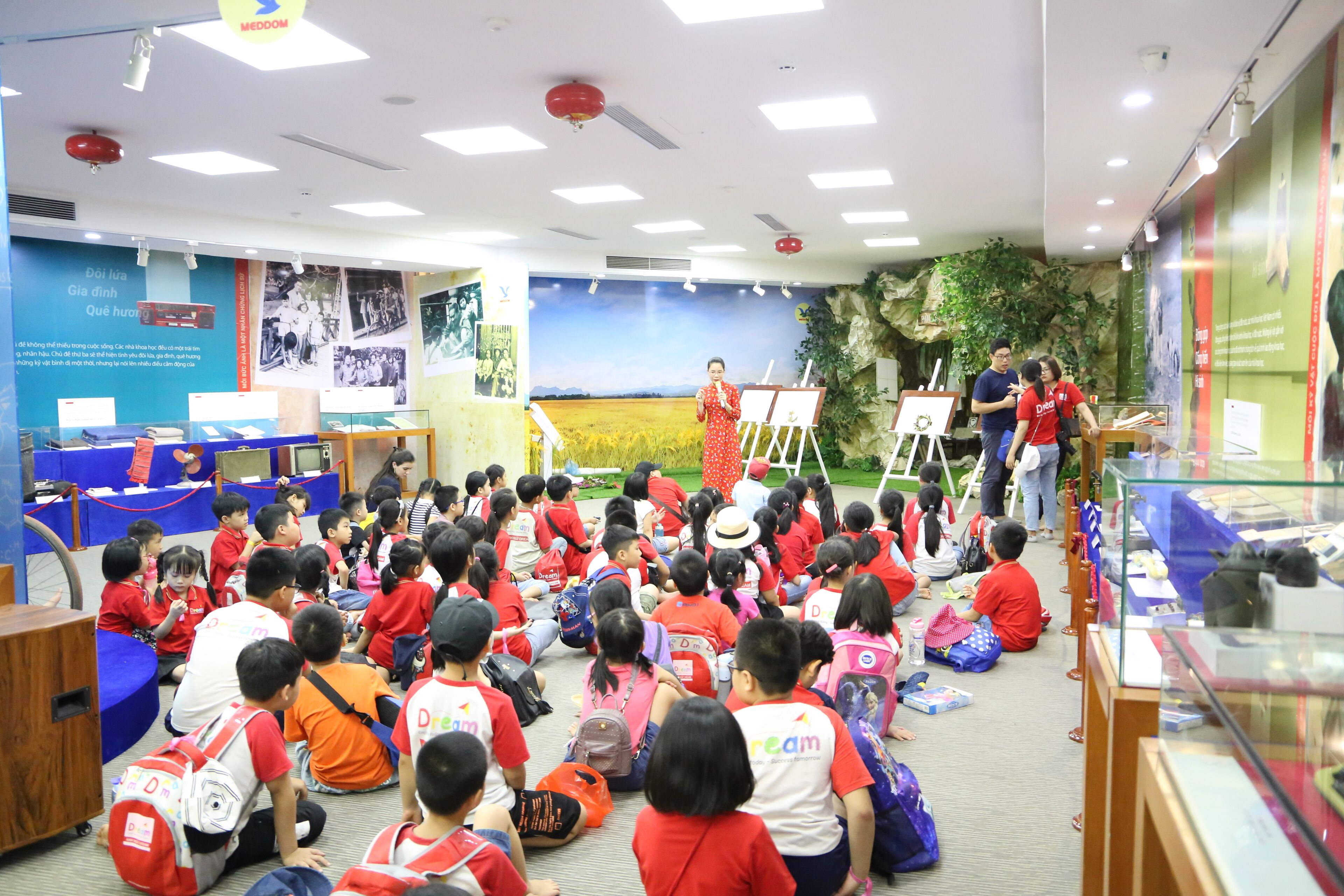 Une salle de classe où les enfants sont assis par terre, face à un enseignant qui se trouve à l’avant de la pièce.