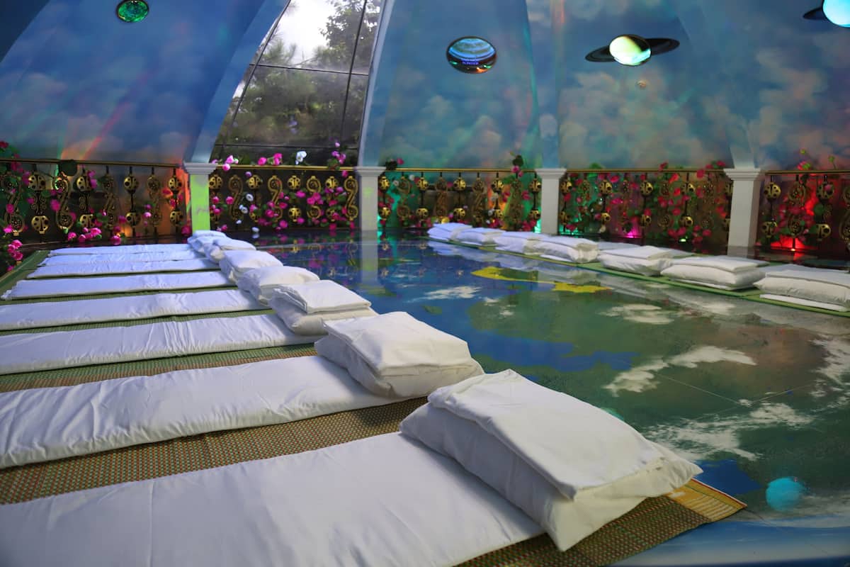 A room with multiple beds arranged in rows, a large window, and a decorative ceiling.