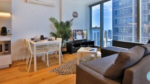 Uma sala de estar moderna com sofá, mesa de jantar, cadeiras, TV e uma grande janela com vista para a cidade.