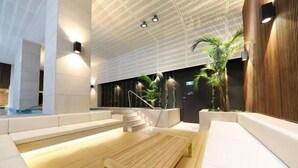 Um lobby moderno com um banco de madeira, sofás brancos e uma escadaria.