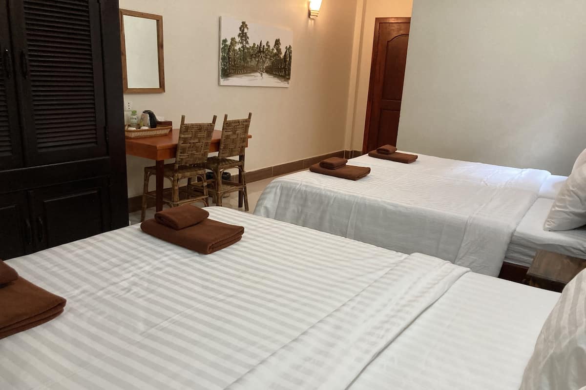 A hotel room with two beds, a dining table with chairs, and a painting on the wall.