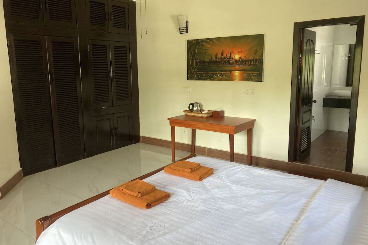 A hotel room with a bed, a wooden table with a tray, a painting, and a wardrobe.