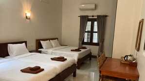 A hotel room with two beds, a wooden table, a chair, a window with curtains, and an air conditioning unit.