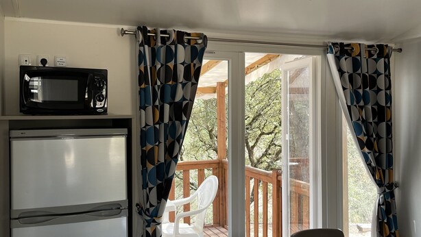 A compact kitchen with a refrigerator, a microwave, and a dining area with a table and chairs. - Mobilhome Gorges de Verdon (Provence-Alpes-Côte d'Azur)