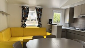 A compact kitchen with a yellow sofa, a round dining table, and a window with curtains. - Mobilhome Gorges de Verdon (Provence-Alpes-Côte d'Azur)