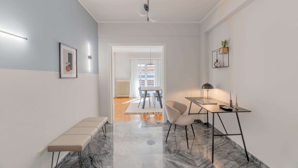 A modern hallway with a bench, a table with a lamp, and a wall-mounted shelf with a plant. - Homey 2BR Apartment in Cholargos (Cholargos)