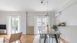 A modern living room with a wooden dining table, blue chairs, a TV, and a radiator. - Homey 2BR Apartment in Cholargos (Cholargos)