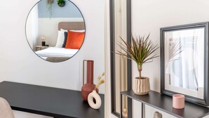 A modern bedroom with a black desk, a round mirror, a potted plant, a framed picture, and a small statue. - Homey 2BR Apartment in Cholargos (Cholargos)