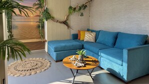 A living room with a blue sectional sofa, a round coffee table with decorative items, and a view of the ocean through a window with vertical blinds. - 5 minutes from the beach/private pool by Gpsrentas (Mazatlán)