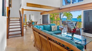 A spacious living area with a large sofa, a glass coffee table, and a view of the ocean. - Oceanfront Luxury House, Pool & AC, Near Magic Sands (Kailua-Kona)
