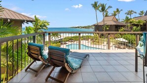 A balcony with two lounge chairs, a pool, and a view of the ocean and resort buildings. - Oceanfront Luxury House, Pool & AC, Near Magic Sands (Kailua-Kona)