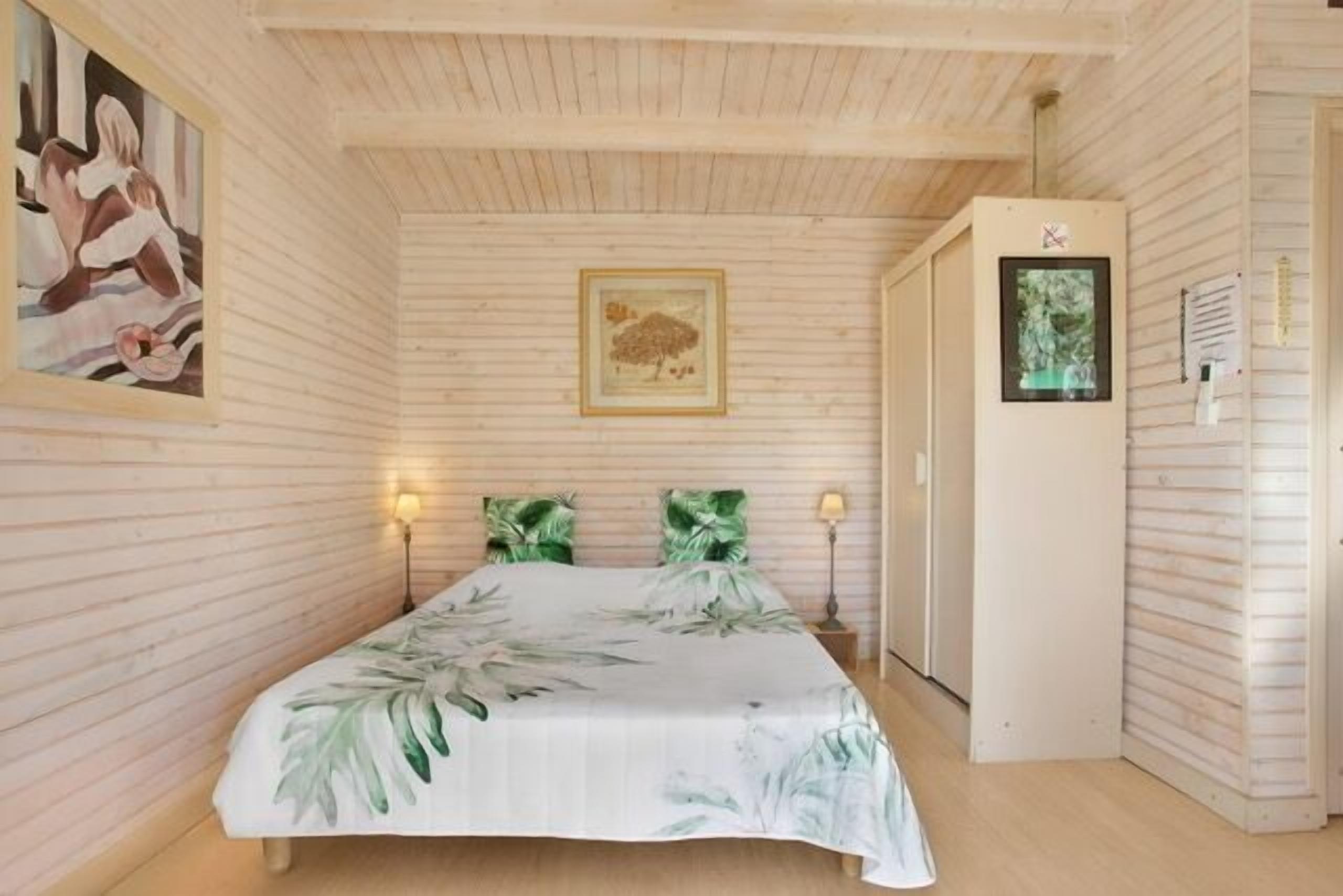 A bedroom with a bed, two wall-mounted lamps, a framed picture, and a door with a sign.