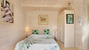 A bedroom with a bed, two wall-mounted lamps, a framed picture, and a door with a sign. - Quiet chalet 10 minutes from the beach (Roquebrune-sur-Argens)