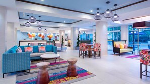A modern hotel lobby with a blue and white color scheme, featuring a reception desk, seating areas, and large windows offering views of the outdoors. - Ocean View! Beachfront Aruba - Family Friendly Resort (Noord)