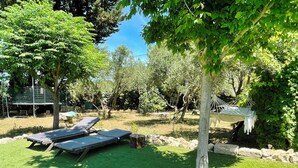 A backyard with two sun loungers, a hammock, and a stone wall.