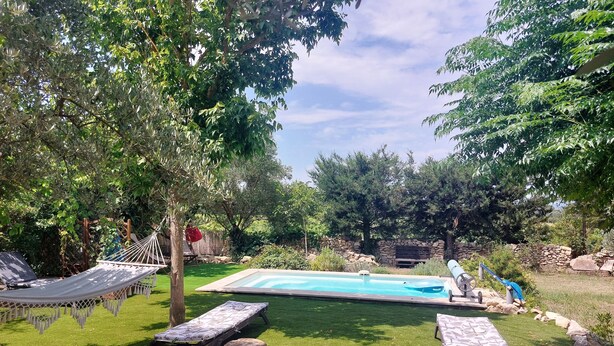 A backyard with a swimming pool, two lounge chairs, a hammock, and a wooden deck.