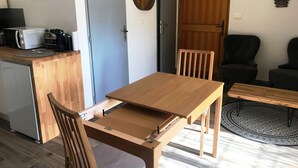 A compact living space with a wooden dining table and chairs, a kitchenette with a microwave and coffee maker, and a round rug.