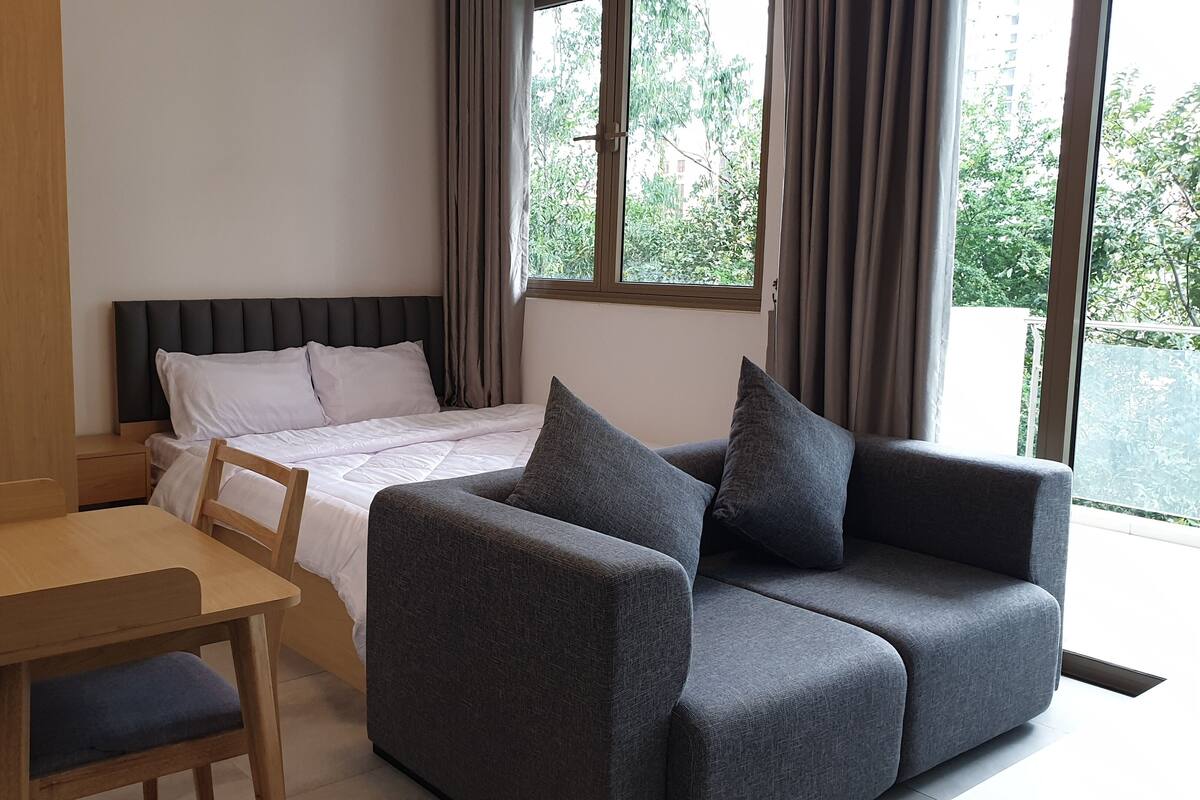 A bedroom with a bed, a grey sofa, a wooden desk, and a window with curtains.