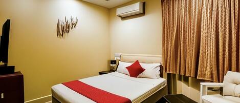 A hotel room with a bed, a desk, a chair, a ceiling fan, and an air conditioning unit.