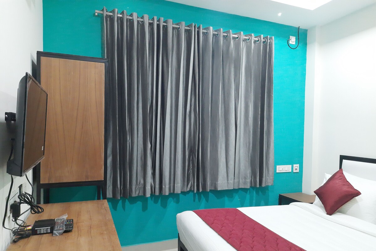 Una habitación con cama, un escritorio de madera, televisor y cortina.