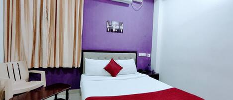 Habitación de hotel con cama, una silla, mesita de noche, equipo de aire acondicionado y pared morada.