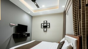 A modern hotel room with a bed, a flat-screen TV, a wall-mounted picture frame, and a ceiling fan. - Naadi stayinn New Busstand Thanjavur (Thanjavur)