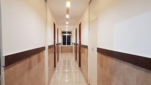 A long, narrow hallway with a shiny, reflective floor and walls with a dark baseboard. - Naadi stayinn New Busstand Thanjavur (Thanjavur)