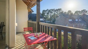 Ein Balkon mit rotem Tisch und Stühlen, mit Blick auf ein Steinhaus und Bäume.