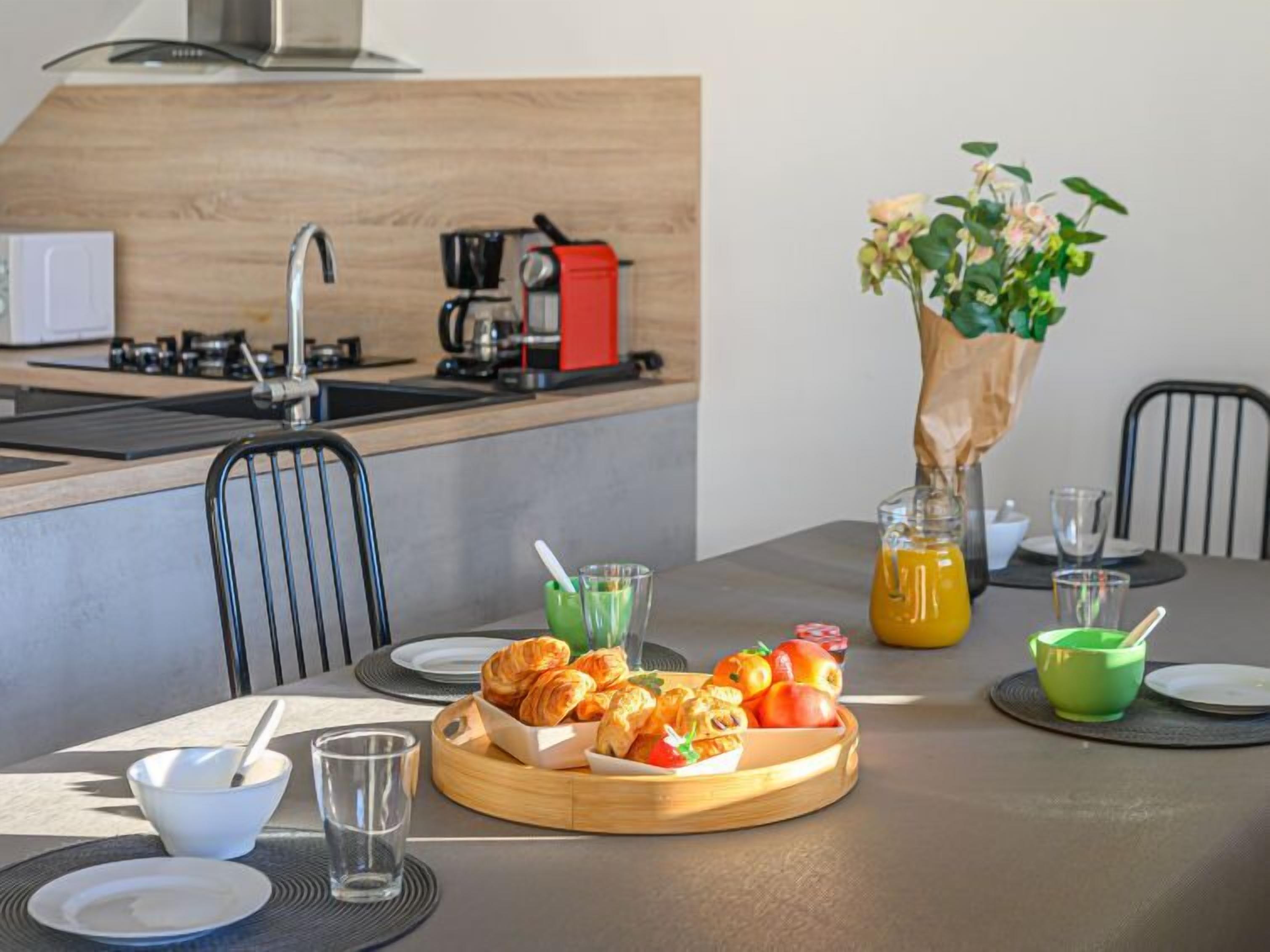 A modern kitchen with a central island, a dining table with breakfast items, and a coffee machine.
