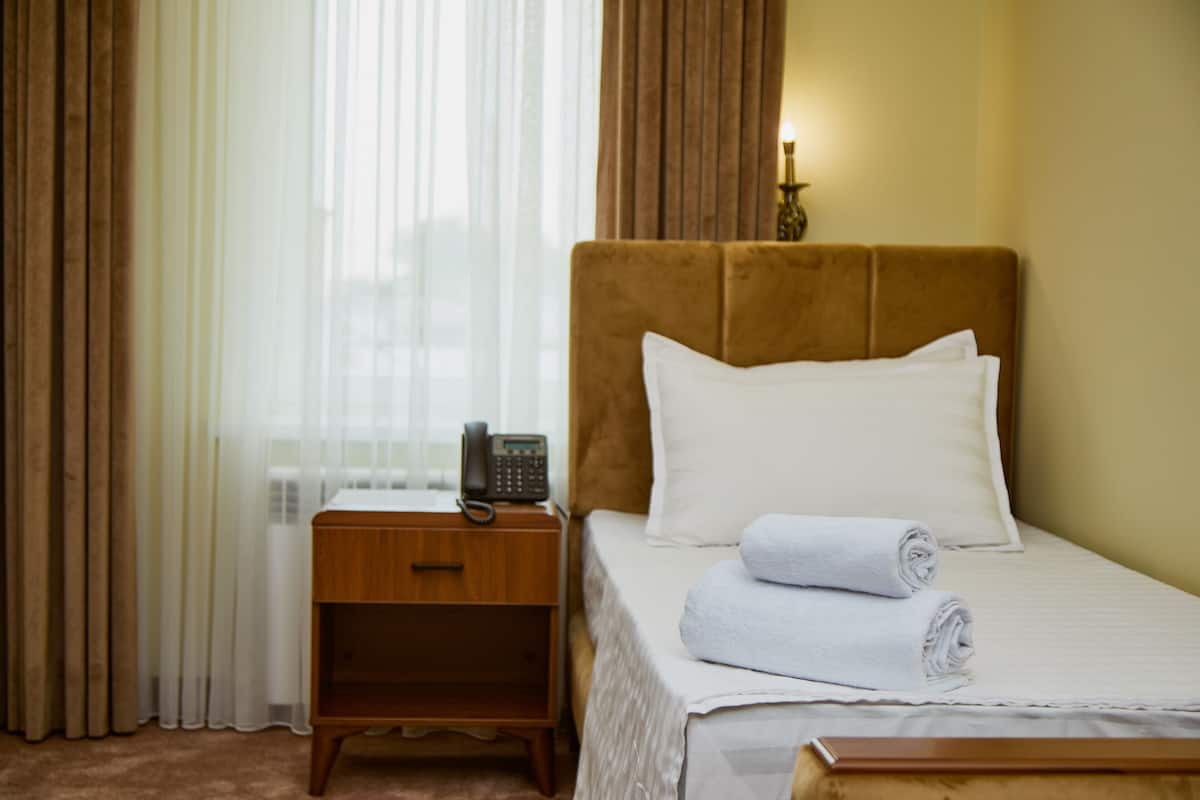 A hotel room with a bed, a bedside table with a phone, and a window with curtains.