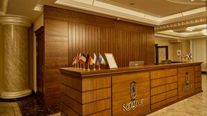 A reception desk with a wooden finish, multiple flags, and a logo. - Sangzor Boutique Hotel (Samarkand)